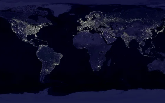 Eine Weltkarte bei Nacht aus dem Weltraum. Helle Lichter markieren die städtischen Gebiete und Kontinente Nord- und Südamerika, Europa, Afrika, Asien sowie Australien vor dem dunklen Hintergrund der Ozeane.